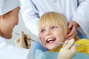 Image of little girl having her teeth checked by doctor and assistant